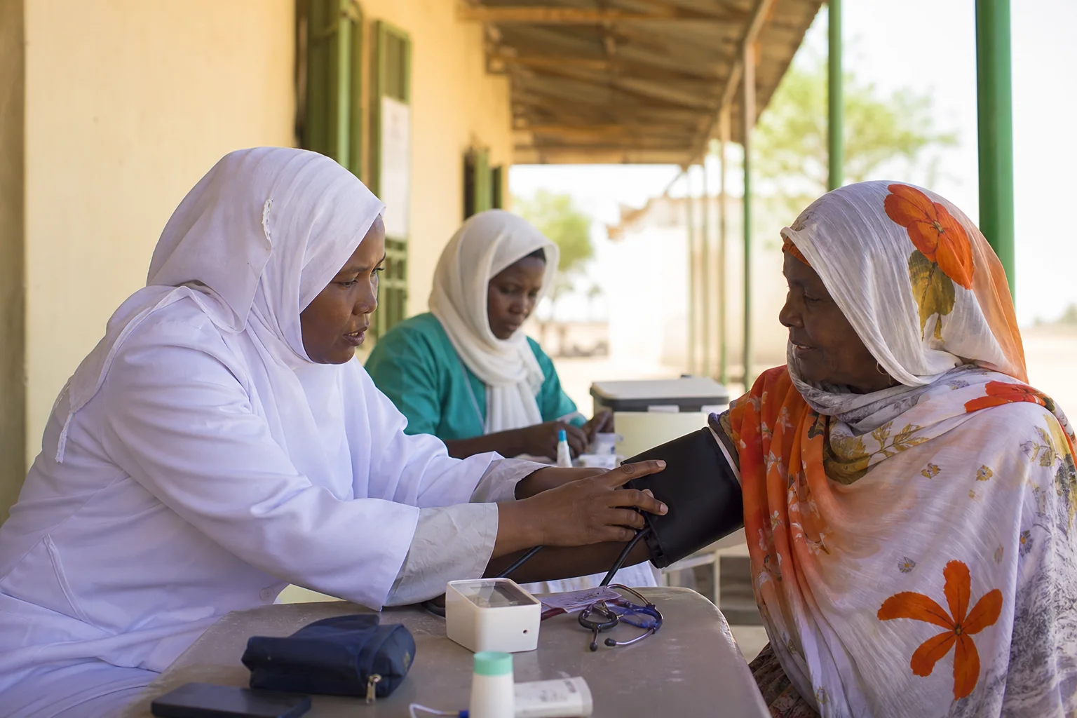A Sudanese nurse checks an older woman’s blood pressure during community health outreach.